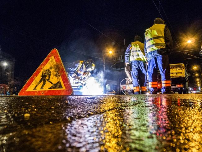 Low angle view of street workers and a welder while repairing the rail tracks in the city at night. Road sign is in front and truck with equipment is in the background. Photo: iStock