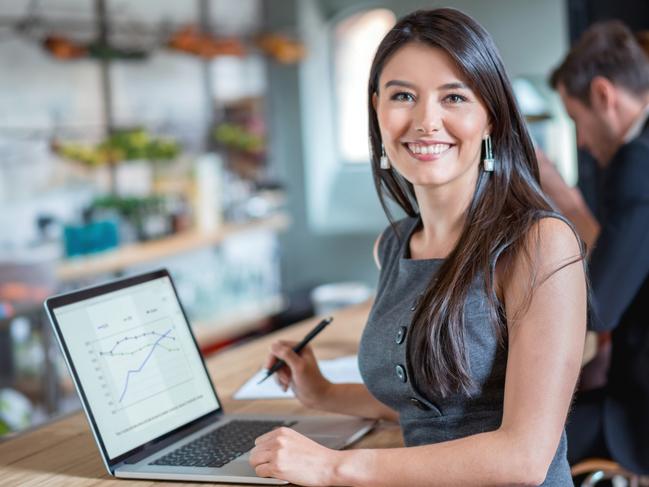 Happy business woman working at a cafe on a laptop and looking at the camera smiling. Image on screen is own design. Investor generic