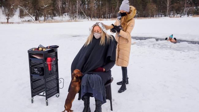 A hairdresser cuts hair on the frozen lake Babelitis while a winter swimmer takes a dip in an ice hole in Riga, Latvia. Hairdressers are not allowed to work due to the pandemic. Picture: AFP