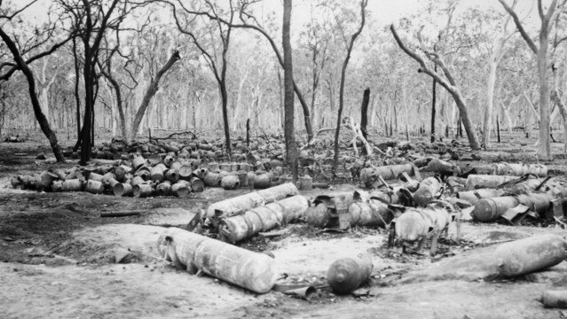 Large cylinders used to contain chemical agents, and hundreds of contaminated drums used for vaporising mustard gas lie on the ground in burnt bush. Credit: Australian War Memorial