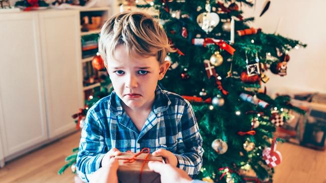 RendezView. Boy wears pajamas and stands before a decorated Christmas tree on Christmas morning. He gets a present and looks sad and unhappy. (Pic: iStock)