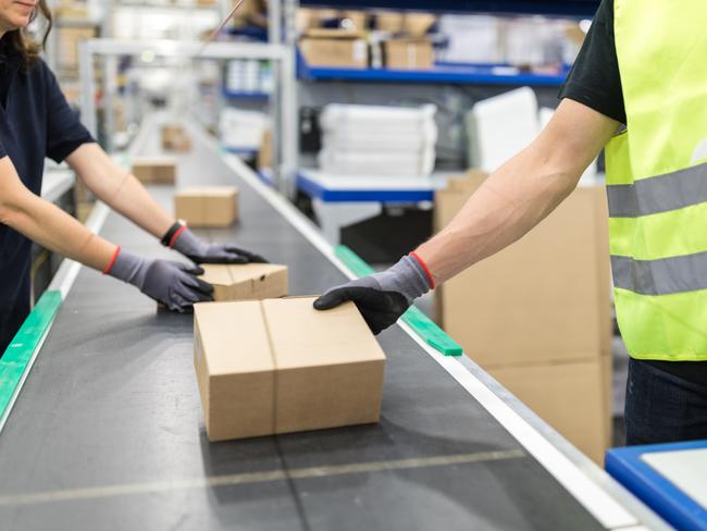 Workers working on conveyor belt in packaging plant. Cropped shot of worker hands takes parcel from moving belt conveyor at distribution warehouse Picture: Istock