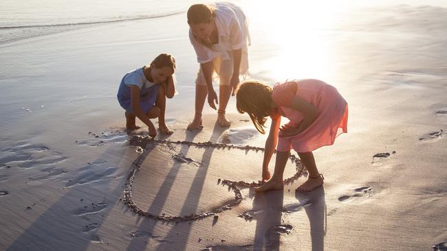 Mother and daughters playing together making heart shapes on a beach at sunset