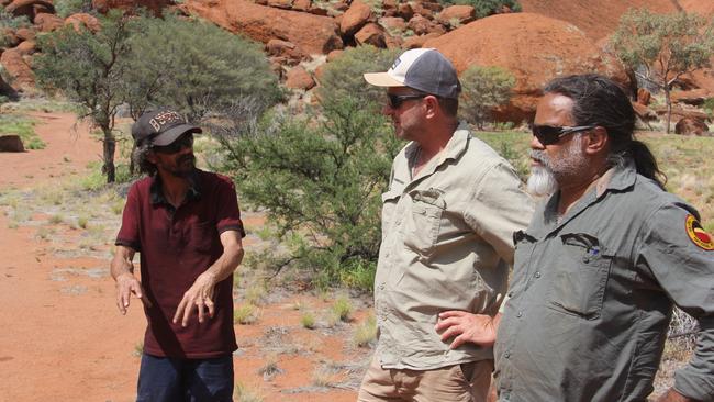 Arrernte Man and Stride Resources director Paddy Laughton talks to NT Regional Weeds Manager Chris Brown and James Aitken from Parks Australia at the base of Uluru. Picture: Supplied