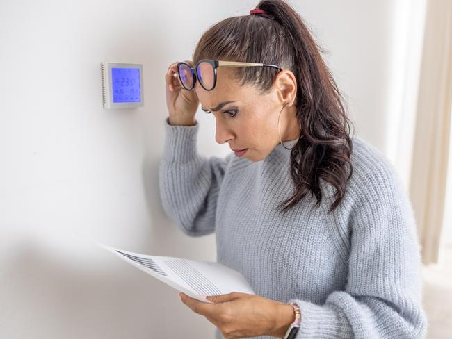 Woman standing next to a thermostat cannot believe the price for heating on her bill. Bill shock generic