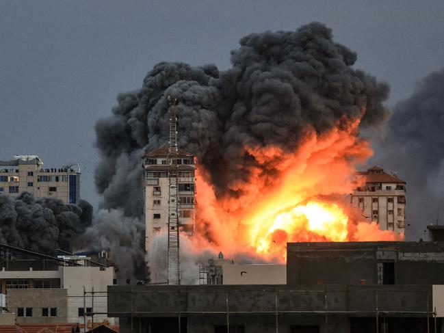 EDITORS NOTE: Graphic content / TOPSHOT - People standing on a rooftop watch as a ball of fire and smoke rises above a building in Gaza City on October 7, 2023 during an Israeli air strike. At least 70 people were reported killed in Israel, while Gaza authorities released a death toll of 198 in the bloodiest escalation in the wider conflict since May 2021, with hundreds more wounded on both sides. (Photo by MAHMUD HAMS / AFP)