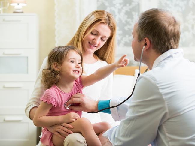 Male Pediatrician examining cute little girl with stethoscope. Kid happily smiling and pointing on doctor. Mother holding her kid. Doctor visit his patient at home.