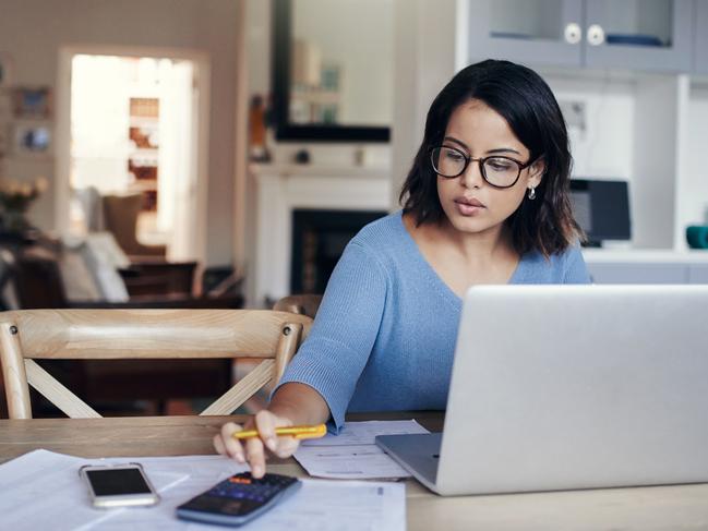 Shot of a young woman using a laptop and calculator while working from home