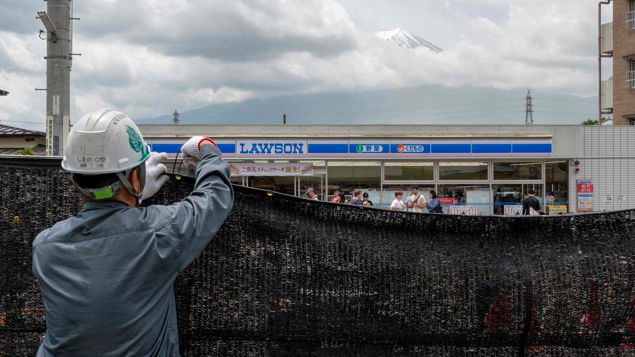 A worker installs a barrier to block the sight of Japan's Mount Fuji across the street from a convenience store in the town of Fujikawaguchiko in May. Picture: Kazuhiro Nogi / AFP