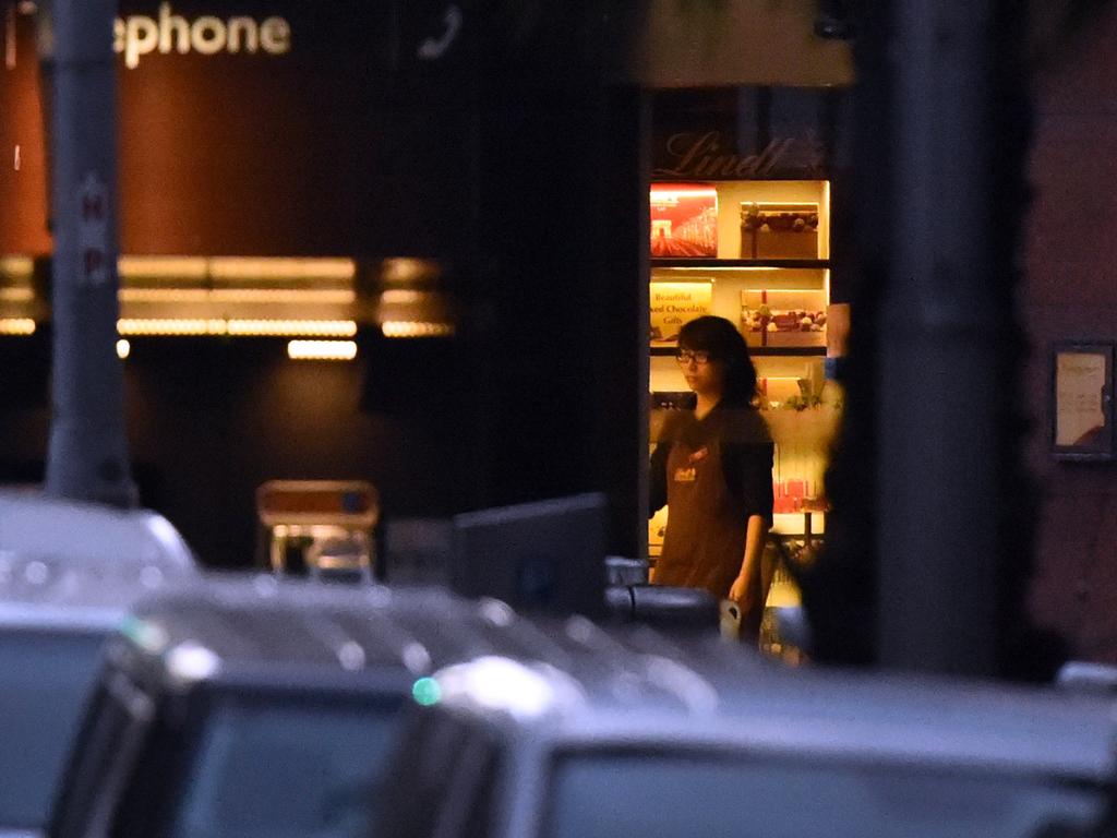 A female hostage stands by the front entrance of the Lindt cafe as she turns the lights off early in a long siege in the Sydney central business district. Picture: William West (AFP)