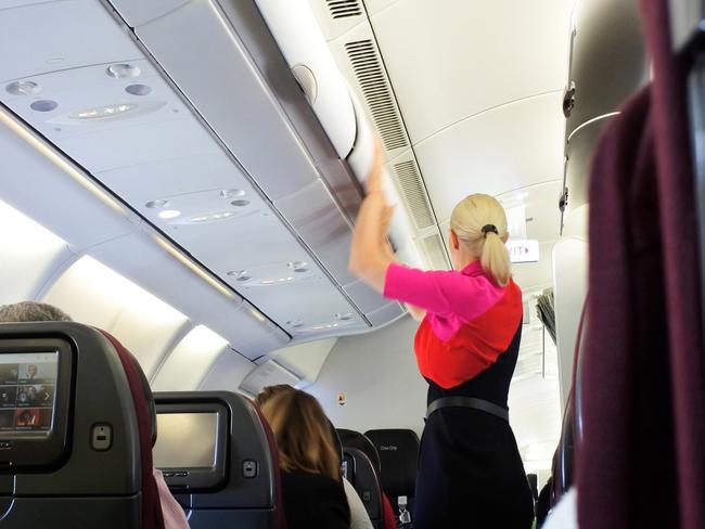Brisbane - Oct 31 2022: Qantas airways female flight attendant closing the overhead luggage compartment lid for carry on baggage before take off.In Australia 1 flight attendant for every 36 passengers.Escape 16 June 2024Why I travelPhoto - iStock