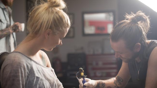 A photo of artist making tattoo on female customer's hand. Tattoo expert is working in studio. Woman looking at man tattooing her hand.