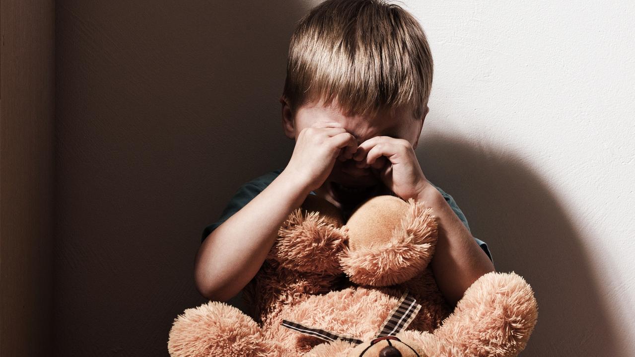 Lonely sad boy crying in corner, holding toy bear