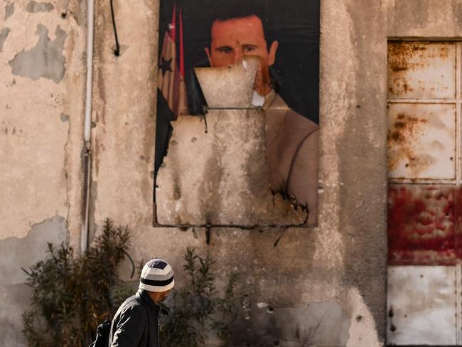 TOPSHOT - A man walks past a defaced portrait of ousted president Bashar al-Assad is pictured in the town of Adra on the northeast outskirts of Damascus on December 16, 2024. Islamist-led rebels took Damascus in a lightning offensive on December 8, ousting president Bashar al-Assad and ending five decades of Baath rule in Syria. (Photo by Aris MESSINIS / AFP)