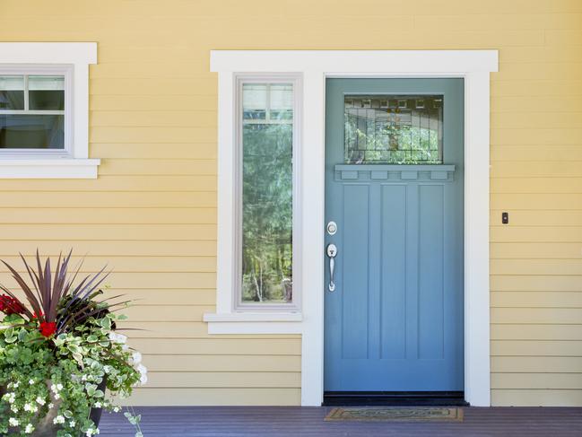 A front entrance of a home with a blue door, yellow siding, and a flowerpot in daytime.