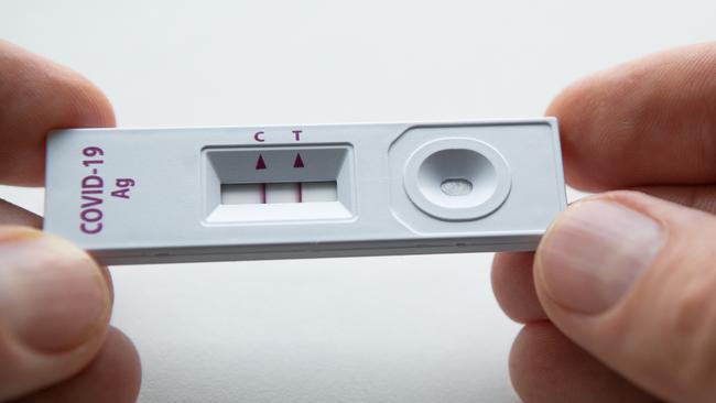 Rapid antigen detection test (RADT) with two red stripes showing a POSITIVE result of a human sample testing. Mans fingers holding the white plastic device with a COVID-19 Ag inscription.