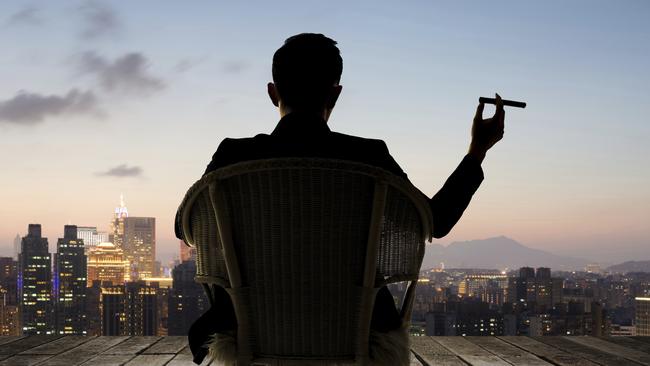 Silhouette of businessman sit on chair and hold a cigar and looking at the city in night.