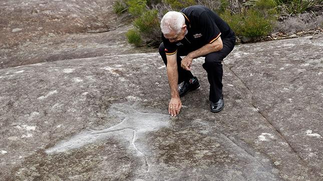 Aboriginal elder Uncle Allen Madden with a rock carving within the Lizard Rock land holding. Picture: Metropolitan Local Aboriginal Land Council