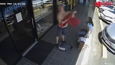 A shirtless man uses a towel to wipe sweat from himself as he stands on the shopping strip.