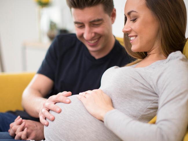 Pregnant Couple Sitting On Sofa With Man Touching Womans Stomach. Picture: iStock