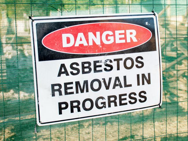 A warning sign Danger Asbestos on a fence at construction site where old house is demolishing  - picture istock