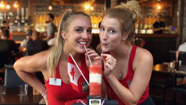 Jessie Moore (left) and Makenna Adams, bar staff at House of Brews in Surfers Paradise, with their special Games concoction which is a mix of Strawberry Daiquiri and Pina Colada served on a medal dais. The bar is the official home of Canada during the Games.