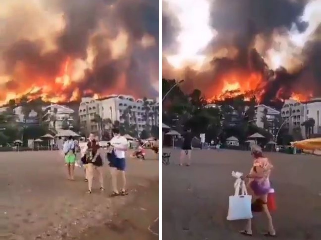 Tourists walk by as a massive fire burns in Turkey.