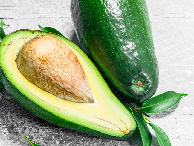 Ripe avocado with leaves. On white rustic background.