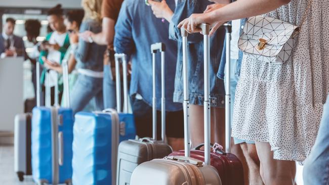 Travelers with luggage using smart phones while waiting in line for boarding at airport. Focus on wheeled luggage.