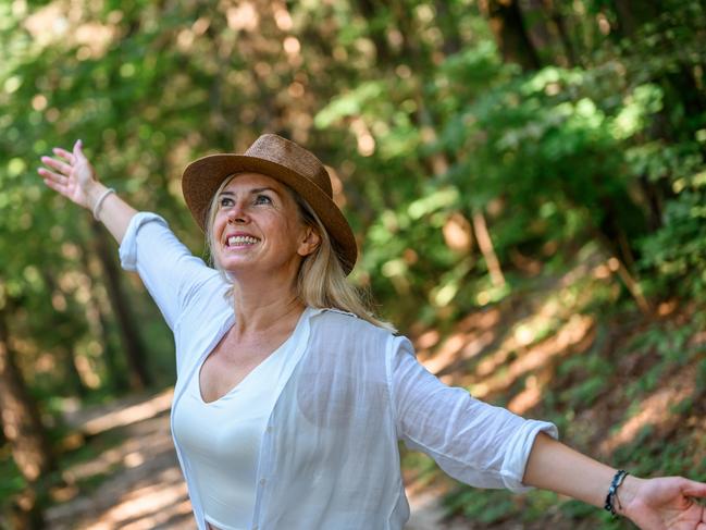 Adult woman with long blond hair and a straw hat, wearing light summer clothes, enjoying summertime in the woods. Middle-aged early retirees generic