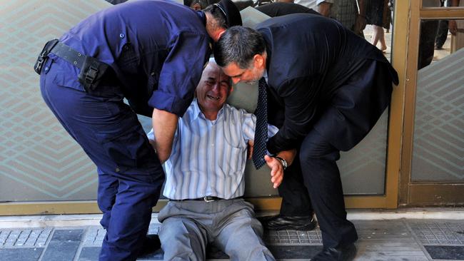 Giorgos Chatzifotiadis is assisted by an employee and a policeman as he sits on the ground outside a national bank branch, as pensioners queue to withdraw their pensions.