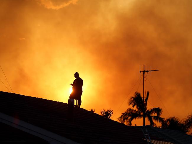 Sunday Telegraph. A home owner keeps an eye out for floating embers from a bushfire threatening houses at Tuncurry on the NSW mid north coast.  Picture Nathan Edwards
