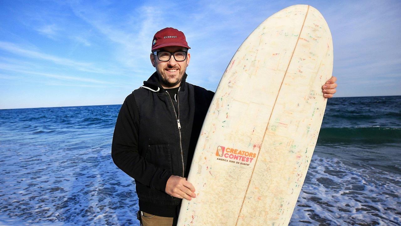 Korey Nolan of Hampton Falls, N.H., stands with the surfboard he made using hundreds of Dunkin' Donuts coffee cups and other single-use materials