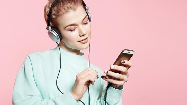 Beautiful young woman in headphones listening to music smiling with closed eyes standing on a pink background in a blue sweatshirt