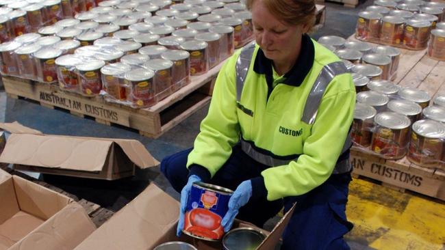 An Australian Customs Service agent unpacks the canned tomato tins holding millions of ecstasy tablets at a warehouse in Melbourne. Picture: AP Photo/Australian Customs Service