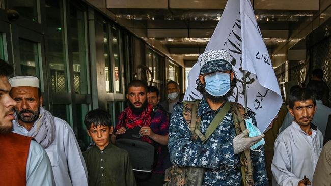 A Taliban fighter stands guard as people move past him at a market with currency exchange in Kabul. Picture: AFP