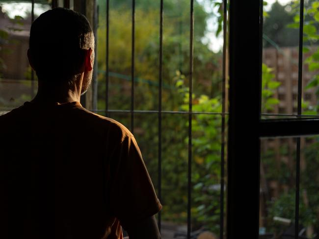 Madrid, Spain. A man with his back turned, backlit, contemplating the first light of day from his bedroom window facing the garden.