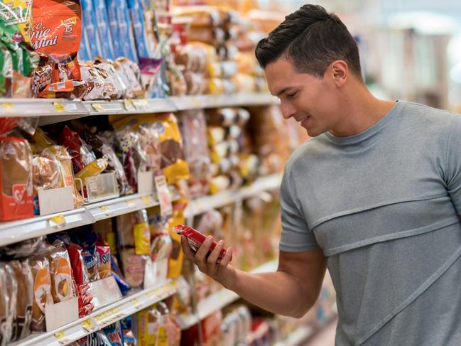 Young single man buying groceries at the supermarket reading the label of a product looking very happy and smiling
