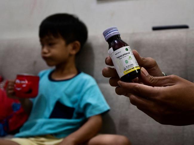 This picture taken on February 11, 2023 shows Riski Agri (R) displaying a bottle of cough syrup that was consumed by his son Farrazka which caused him kidney problems, at their house in Jakarta. - Five-year-old Farrazka was required to undergo dialysis for his failing kidneys after he took the medicines, his mother Indah Septian told AFP. (Photo by BAY ISMOYO / AFP) / To go with "Indonesia-pharmaceutical-children-health", FOCUS by Gemma CAHYA