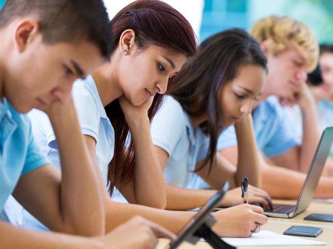 Schools of excellence - Row of private high school students work on assignment in class. They are writing or using laptops or digital tablets. They are concentrating as they study. They are wearing school uniforms.