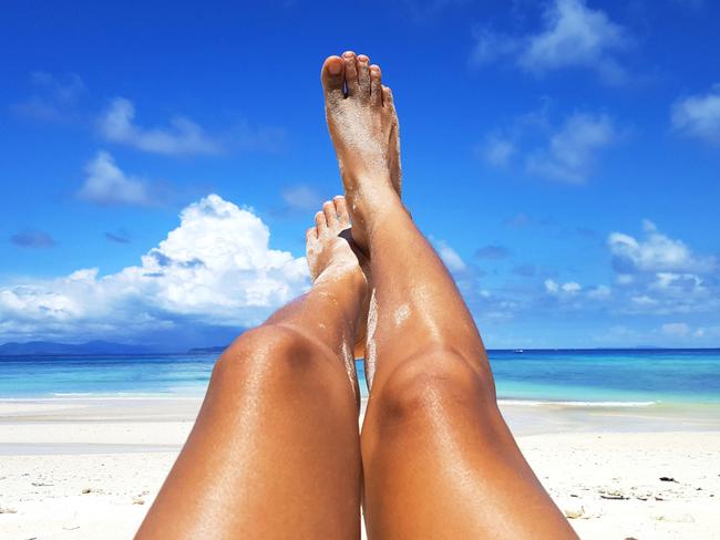 Woman tanned skin legs sunbathing on the white sand beach with the blue sky and sea in the background, Summer holidays and vacations concept.  - picture iStock