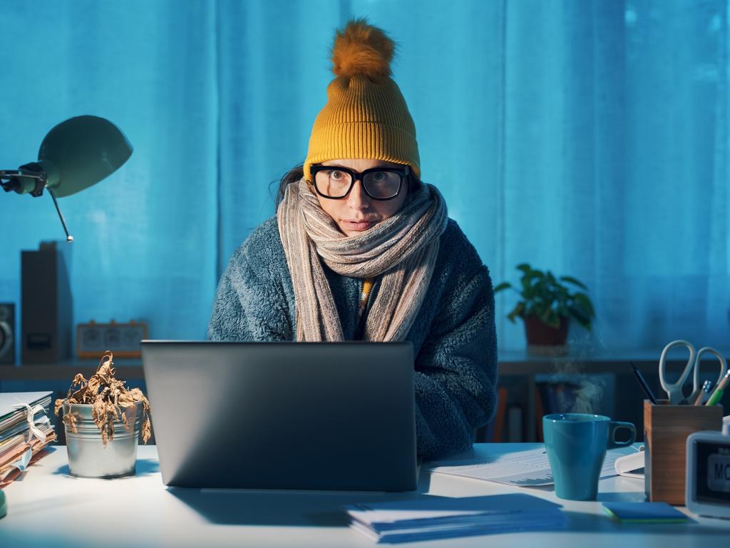 Woman sitting at desk and feeling cold, she is wearing warm clothes and saving money on her utility bills, electricity generic winter