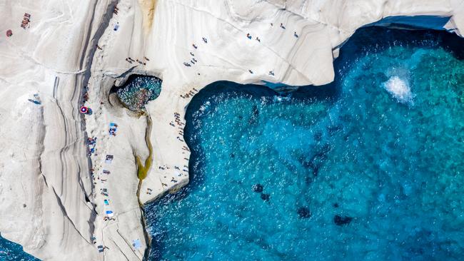 The chalk rock formations of Sarakiniko with people enjoying the sparkling blue sea on a hot summer day, Milos island, Cyclades, Greece.