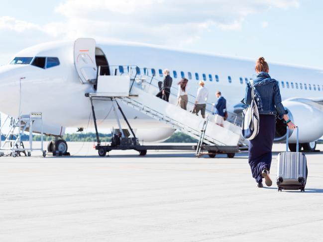 Rear view of young woman with luggage walking towards the airplane. Female traveler going on vacation.Escape 28 July 2024Cover StoryPhoto - iStock