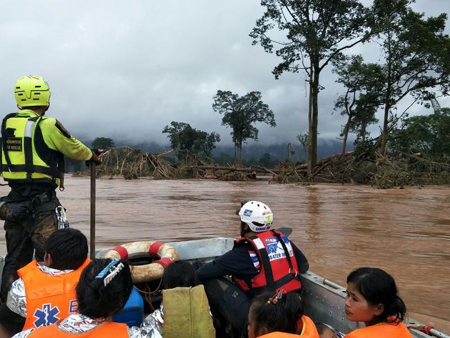 This handout photo from the Thai Rescue Team shows a member of the team riding in a raft with rescued flood survivors close to the swollen river in Attapeu province. Picture: AFP