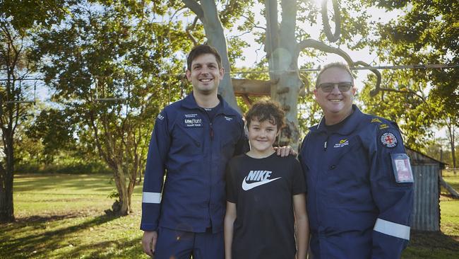 LifeFlight Critical Care Doctor Richard Parker, the 13-year-old boy he saved in March Eli Jarick, and Queensland Ambulance Service (QAS) Flight Paramedic Kevin Charteris in front of the tree Eli fell from in his backyard.