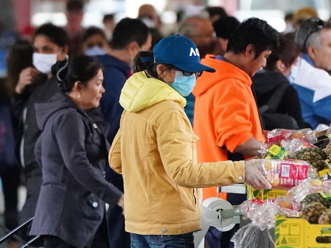 People shop at the Queen Victoria Market while wearing  face masks as a preventive measure against the spread of novel coronavirus COVID-19 in Melbourne, Saturday, April 11, 2020. Authorities have said social distancing and isolation measures could still remain in place for the next six months.  A shutdown of non-essential services is in effect Australia wide in a bid to slow the spread of the coronavirus (COVID-19) disease. (AAP Image/Scott Barbour) NO ARCHIVING