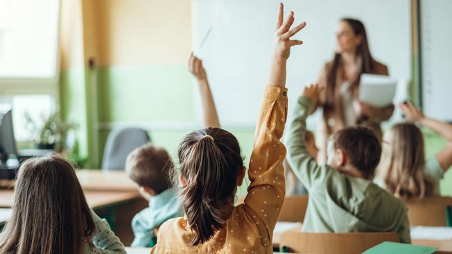 Students raising hands while teacher asking them questions in classroom