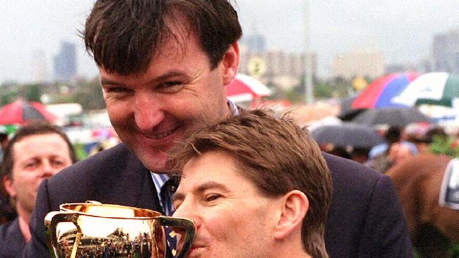 Jockey Wayne Harris kisses Melbourne Cup trophy as trainer of racehorse Jeune, David Hayes looks on. 1 November 1994          Sport / Turf / Trophies