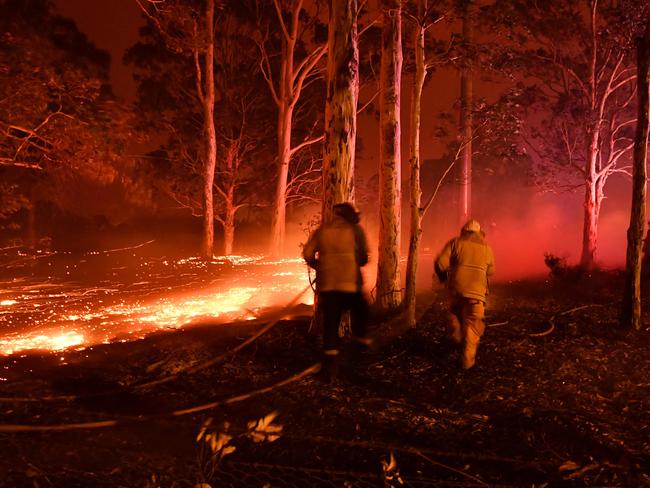 Firefighters hosing down trees as they battle against bushfires around the town of Nowra in the Australian state of New South Wales on December 31, 2019. - Thousands of holidaymakers and locals were forced to flee to beaches in fire-ravaged southeast Australia on December 31, as blazes ripped through popular tourist areas leaving no escape by land. Picture: Saeed Khan/AFP